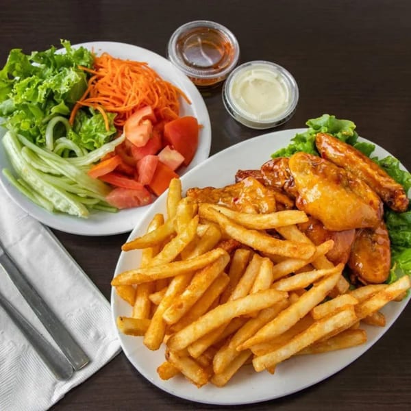 Plates of golden french fries, glazed chicken wings, and a fresh salad with dressing cups.