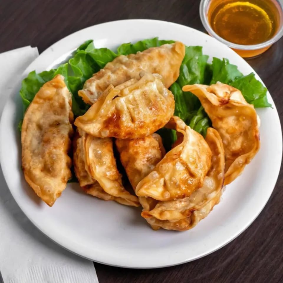 Golden-brown fried dumplings on a bed of green lettuce, with a small cup of dipping sauce.