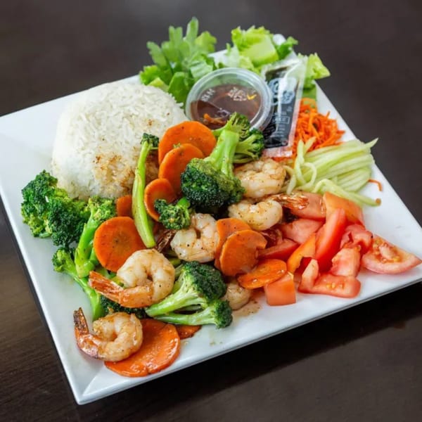 Vietnamese shrimp stir-fry with broccoli, carrots, tomatoes, rice, and a side of sauce.