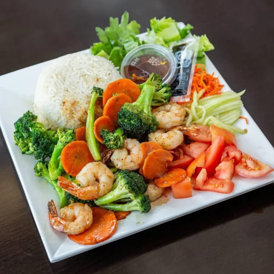 Vietnamese shrimp stir-fry with broccoli, carrots, tomatoes, rice, and a side of sauce.