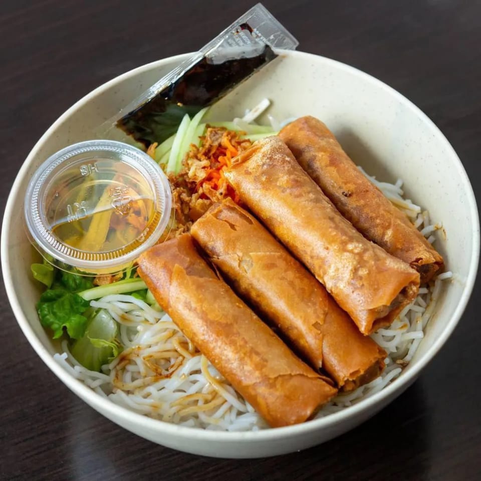Vietnamese vermicelli bowl with four crispy spring rolls, fresh greens, and sauces in a white bowl.