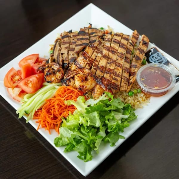 Grilled chicken and shrimp with rice, fresh tomatoes, cucumbers, shredded carrots, and lettuce.