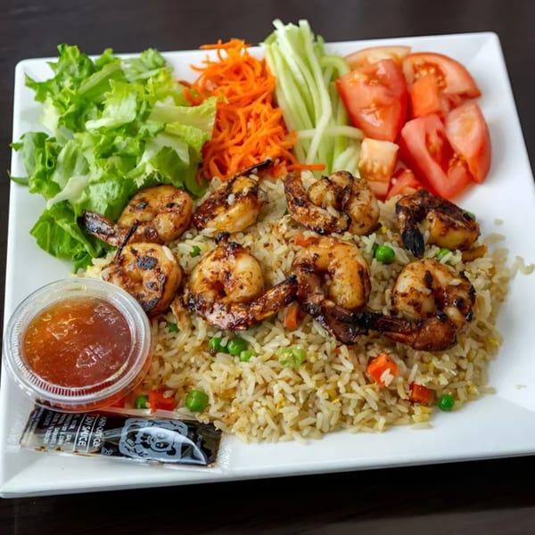 Grilled shrimp and fried rice with a side of salad, shredded carrots, cucumbers, and tomatoes.