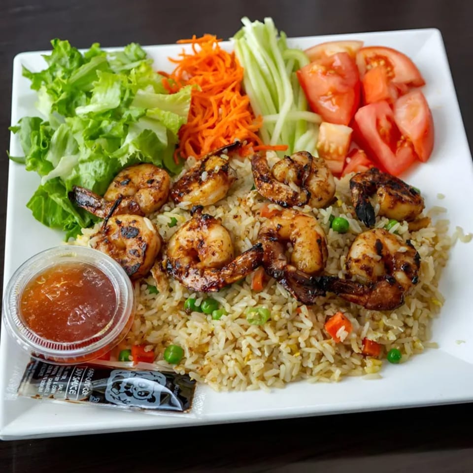 Grilled shrimp and fried rice with a side of salad, shredded carrots, cucumbers, and tomatoes.